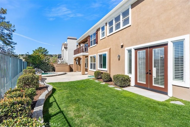 back of house featuring french doors, stucco siding, a lawn, a balcony, and a fenced backyard