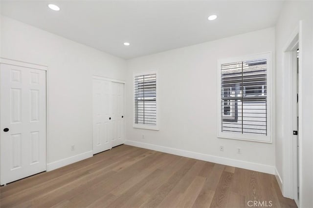 unfurnished bedroom featuring multiple closets, recessed lighting, baseboards, and wood finished floors