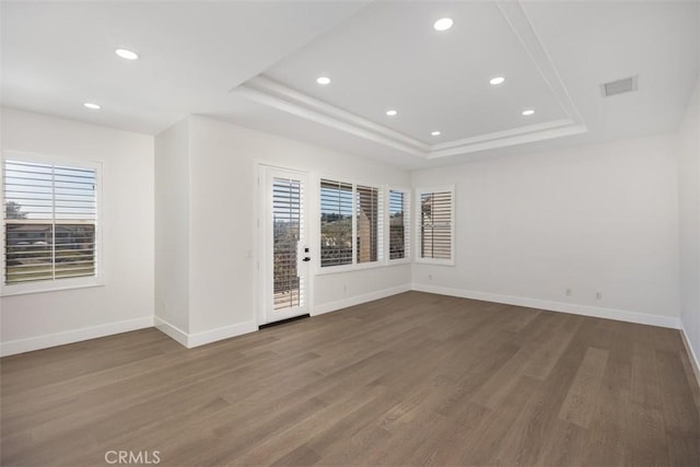 spare room featuring wood finished floors, recessed lighting, a raised ceiling, and baseboards