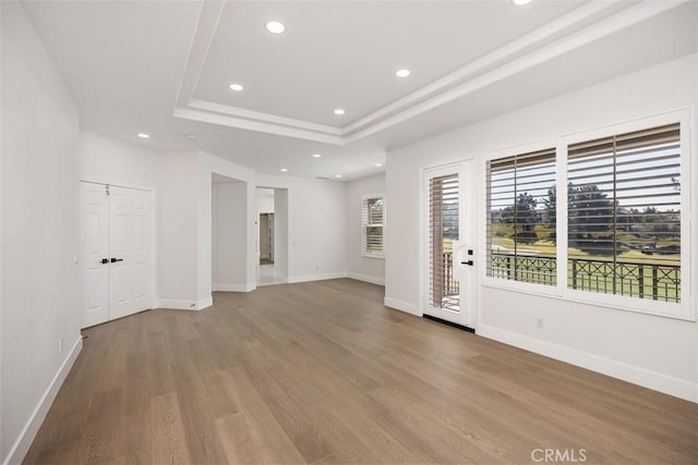 spare room featuring baseboards, a tray ceiling, wood finished floors, and recessed lighting