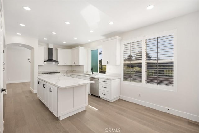 kitchen featuring arched walkways, cooktop, stainless steel dishwasher, a sink, and wall chimney range hood