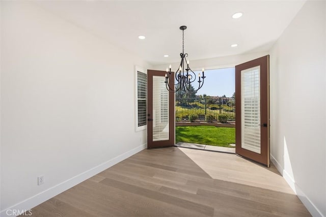 unfurnished dining area featuring an inviting chandelier, baseboards, wood finished floors, and recessed lighting