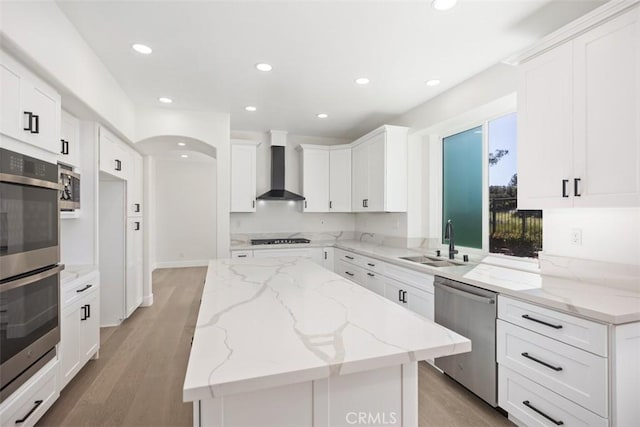 kitchen with wall chimney exhaust hood, a kitchen island, stainless steel appliances, a sink, and recessed lighting