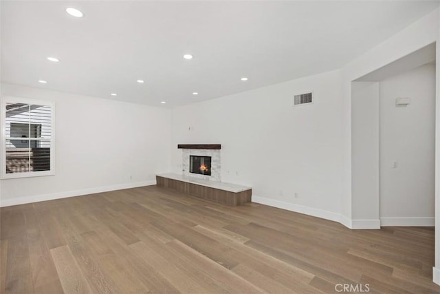 unfurnished living room with baseboards, visible vents, a glass covered fireplace, wood finished floors, and recessed lighting