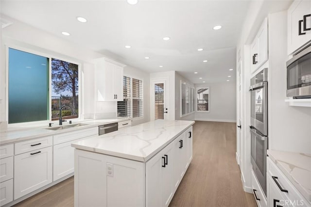 kitchen featuring appliances with stainless steel finishes, a center island, light wood-style floors, and a sink