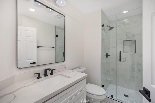 bathroom featuring toilet, a marble finish shower, and vanity