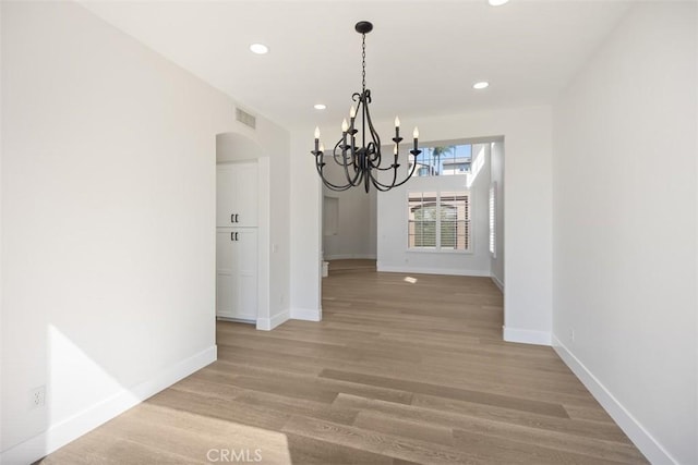 unfurnished dining area featuring arched walkways, wood finished floors, visible vents, and baseboards