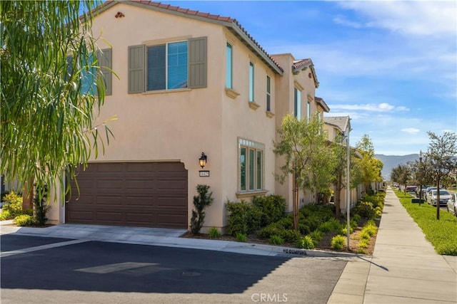 view of front facade with an attached garage, a tile roof, stucco siding, a mountain view, and concrete driveway