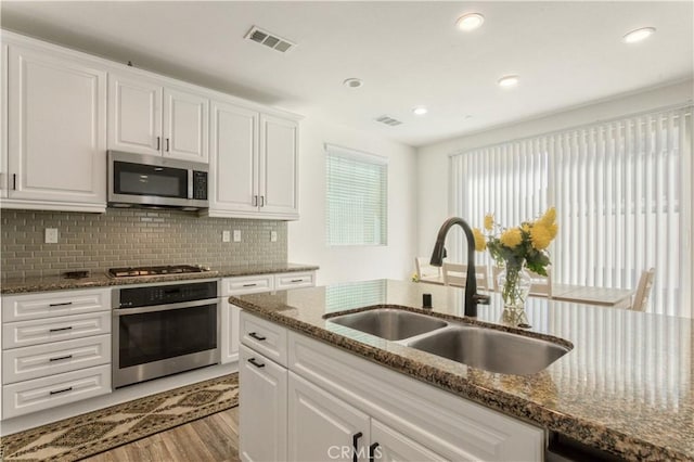 kitchen with a sink, stainless steel appliances, white cabinetry, light wood-type flooring, and visible vents