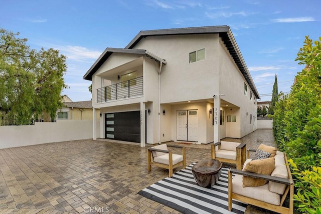 view of front of home with a balcony, fence, stucco siding, a garage, and decorative driveway