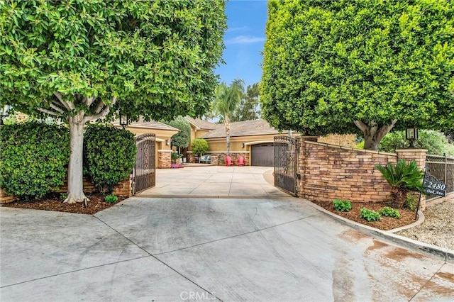 view of property hidden behind natural elements featuring driveway, a tiled roof, a gate, fence, and stucco siding