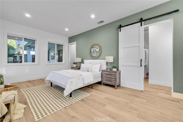 bedroom featuring a barn door, visible vents, light wood-style flooring, and recessed lighting