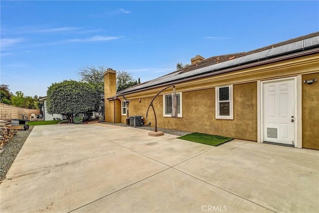 rear view of house with a patio, a chimney, central air condition unit, roof mounted solar panels, and stucco siding