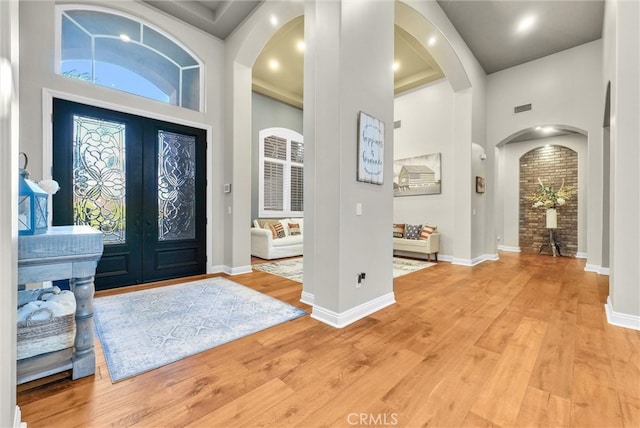 foyer with arched walkways, a high ceiling, baseboards, french doors, and light wood-type flooring