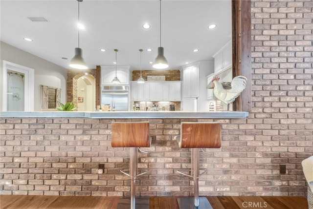 kitchen featuring white cabinetry, stainless steel built in fridge, decorative light fixtures, and wood finished floors