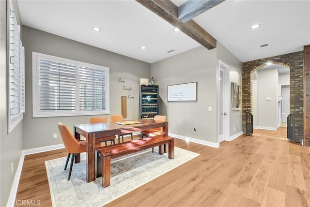 dining area with light wood-style floors, arched walkways, beamed ceiling, and baseboards