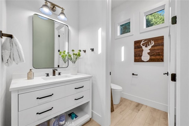 bathroom featuring toilet, baseboards, wood finished floors, and vanity