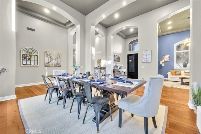 dining room featuring a high ceiling, light wood-type flooring, visible vents, and baseboards