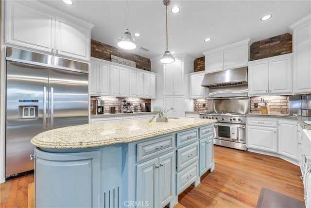 kitchen featuring white cabinets, high end appliances, an island with sink, light wood-style flooring, and under cabinet range hood