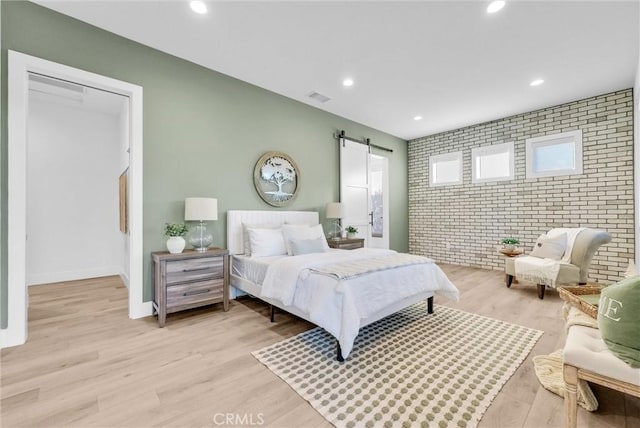 bedroom featuring brick wall, a barn door, light wood-style flooring, and recessed lighting