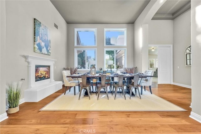 dining space with visible vents, a high ceiling, a glass covered fireplace, wood finished floors, and baseboards