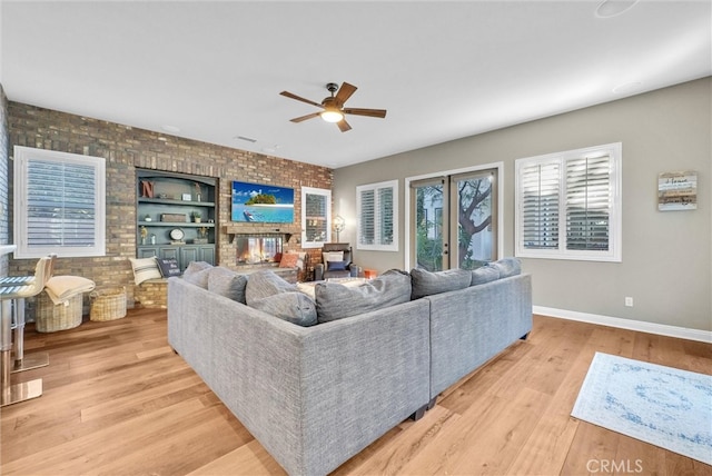 living room featuring baseboards, built in features, a ceiling fan, light wood-style floors, and a fireplace