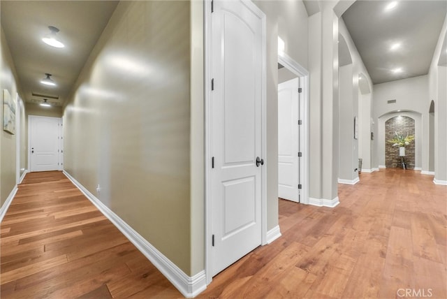 corridor featuring arched walkways, light wood finished floors, and baseboards