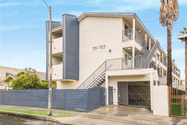 view of property with stairway, an attached garage, fence, and driveway