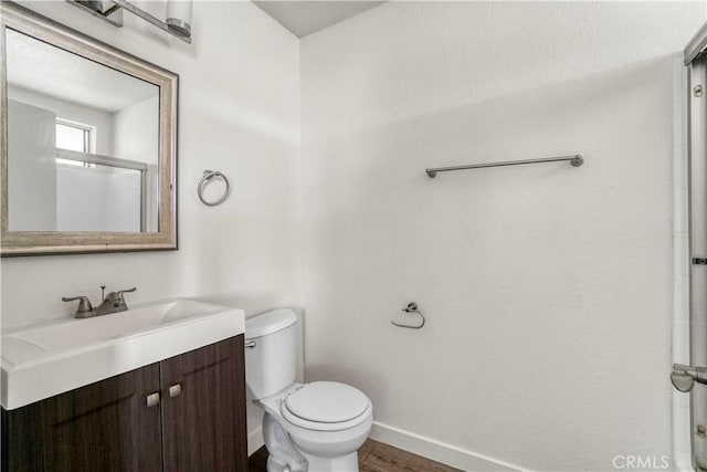 full bath with vanity, wood finished floors, baseboards, walk in shower, and toilet