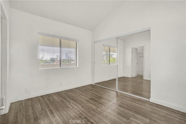 unfurnished bedroom featuring a closet, lofted ceiling, baseboards, and wood finished floors