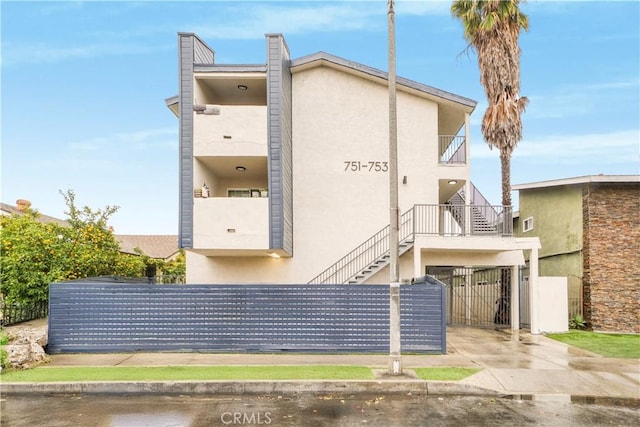 view of side of home featuring stucco siding, stairs, and fence