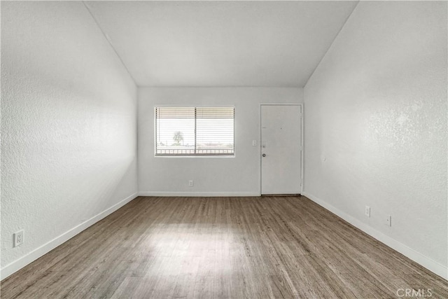 empty room featuring vaulted ceiling, baseboards, and wood finished floors