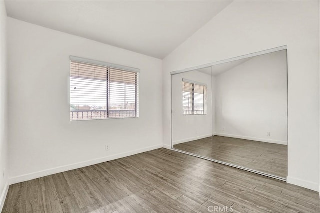 spare room with baseboards, wood finished floors, and vaulted ceiling