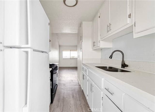 kitchen featuring light wood-style flooring, a sink, black gas stove, white cabinetry, and freestanding refrigerator