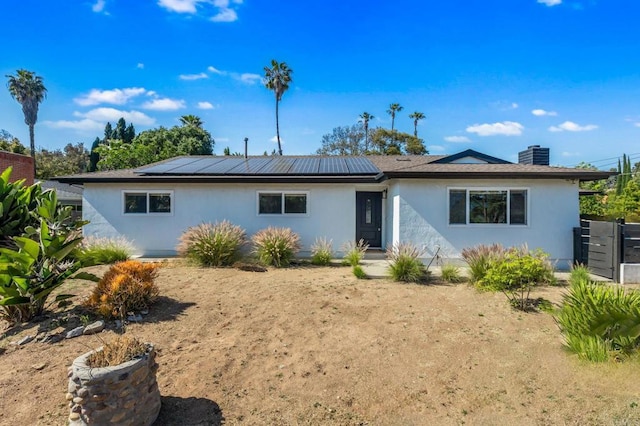 ranch-style home featuring roof mounted solar panels, a chimney, and stucco siding