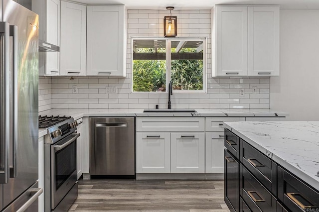 kitchen with tasteful backsplash, wood finished floors, stainless steel appliances, white cabinetry, and a sink