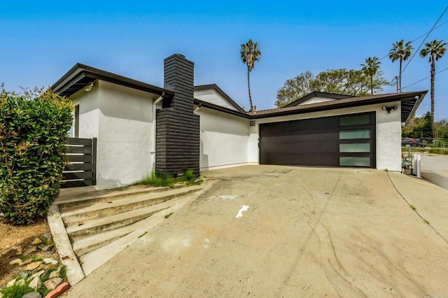 view of front facade featuring a garage, driveway, a chimney, and stucco siding