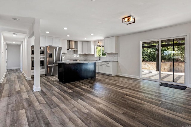 kitchen featuring a sink, wall chimney range hood, appliances with stainless steel finishes, decorative backsplash, and dark wood-style floors