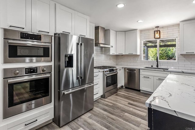 kitchen with stainless steel appliances, tasteful backsplash, a sink, light stone countertops, and wall chimney exhaust hood