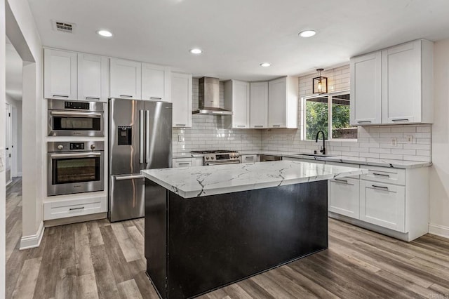 kitchen featuring wood finished floors, a sink, visible vents, appliances with stainless steel finishes, and wall chimney exhaust hood