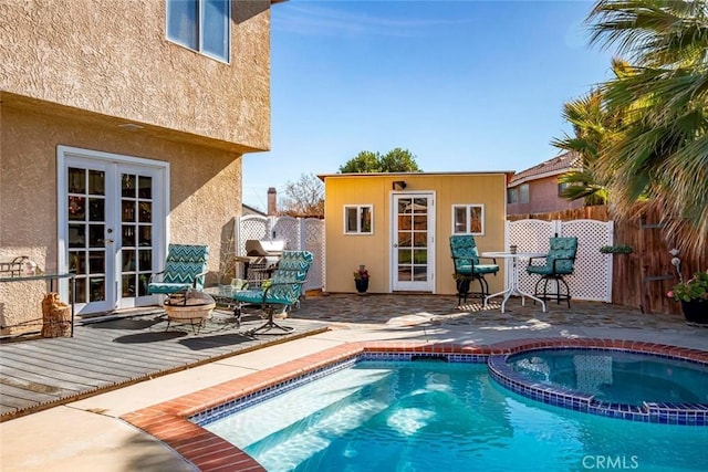 view of pool featuring an outbuilding, french doors, a pool with connected hot tub, a patio area, and fence