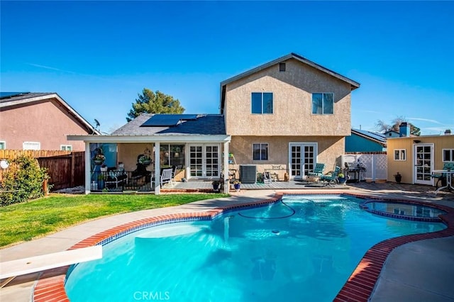 back of property with a fenced backyard, cooling unit, french doors, roof mounted solar panels, and stucco siding