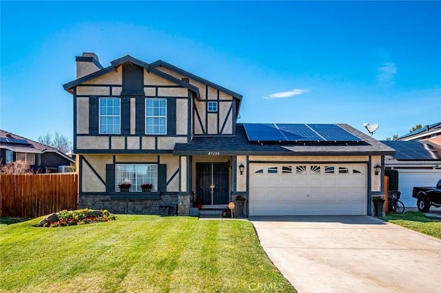 tudor home featuring fence, roof mounted solar panels, a front lawn, a chimney, and stucco siding