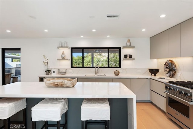 kitchen with visible vents, modern cabinets, a kitchen breakfast bar, high end stainless steel range oven, and a sink