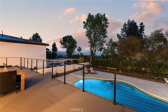 pool at dusk featuring an outdoor pool and a patio area