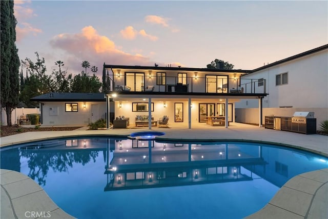 back of property at dusk featuring a balcony, outdoor lounge area, area for grilling, a pool with connected hot tub, and a patio area