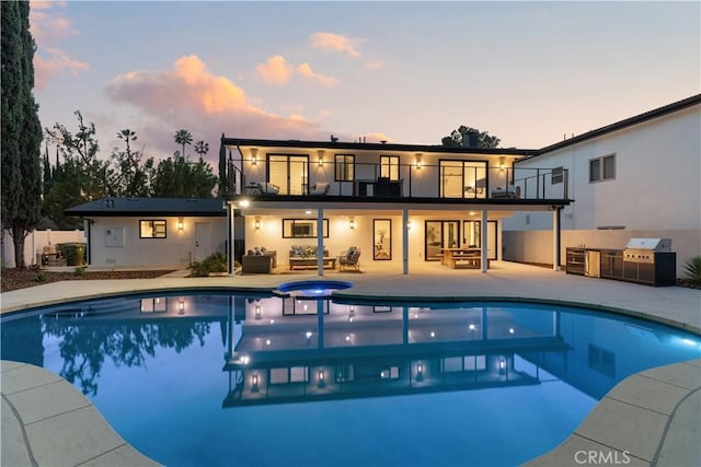 back of property at dusk featuring area for grilling, an outdoor pool, a patio area, an outdoor hangout area, and a balcony
