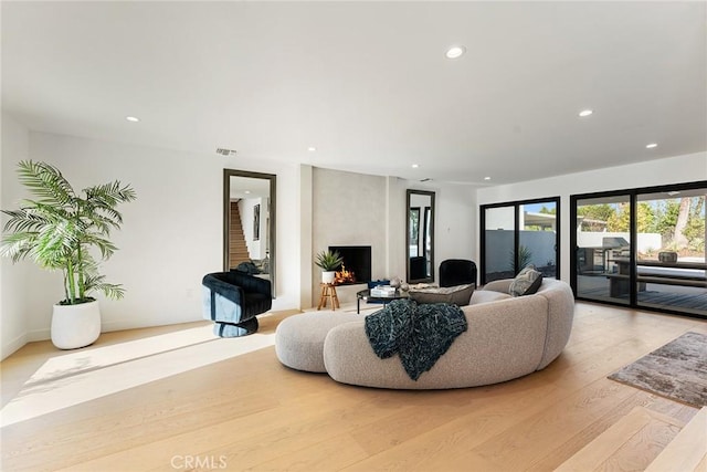 living room featuring light wood-type flooring, a fireplace, visible vents, and recessed lighting