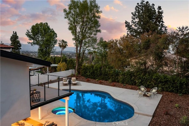 pool at dusk featuring a patio and a pool with connected hot tub