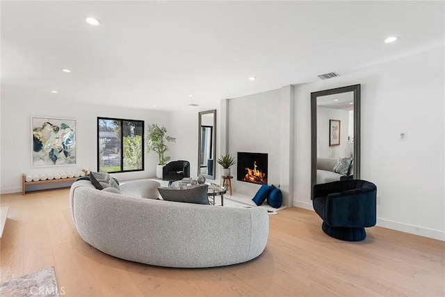 living room with light wood-style floors, recessed lighting, and a warm lit fireplace